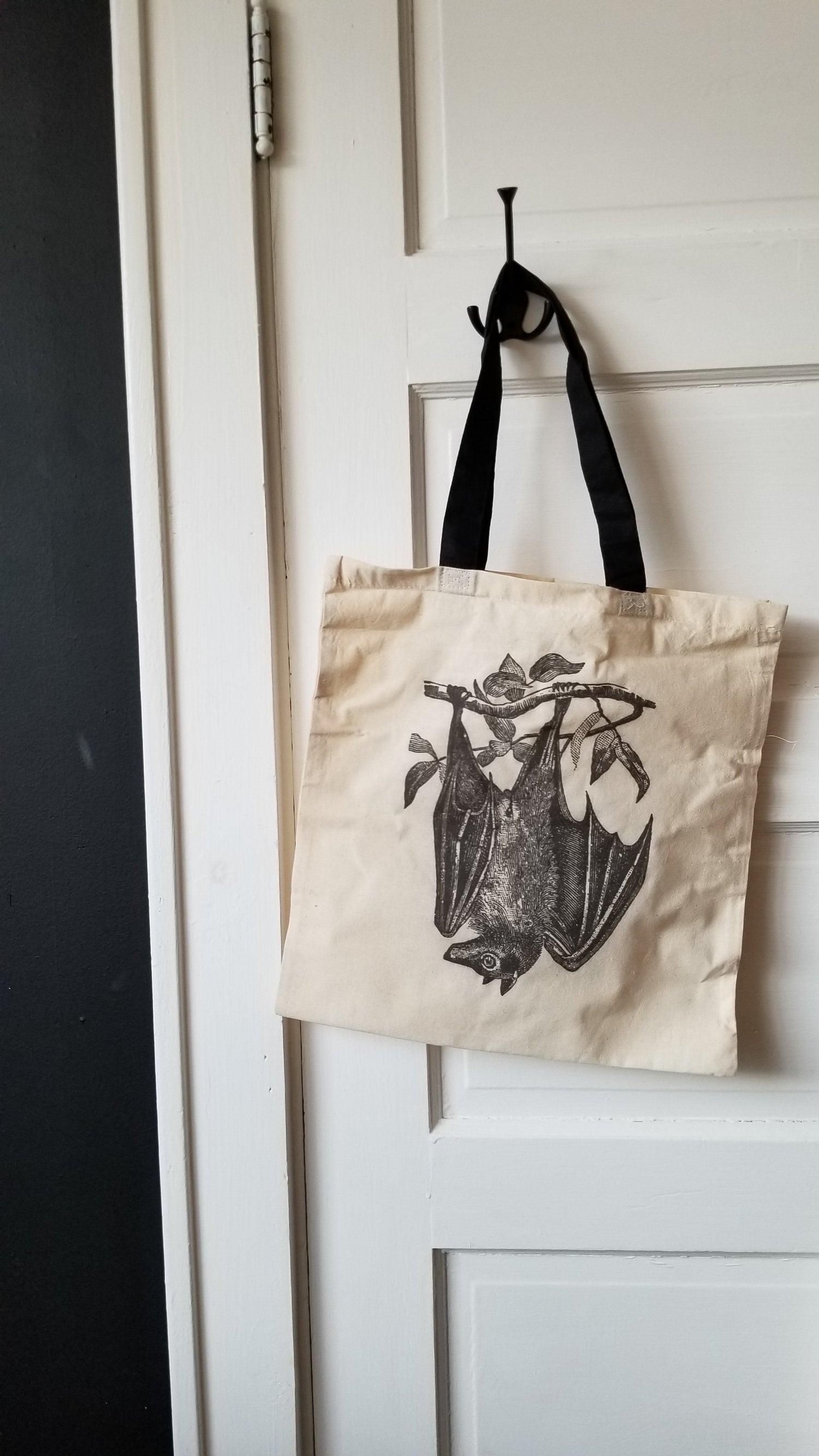 Black Sketch illustration of a Fruitbat hanging upside down from a branch, printed on a cream canvas totebag with a black handle.